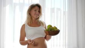 eating pregnant belly nude - nutrition during pregnancy, female with a big tummy eats grapes from a  wooden plate at