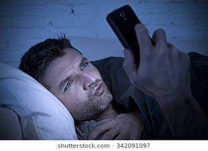 low 20s porn - young man in bed couch at home late at night with intense face expression  using mobile