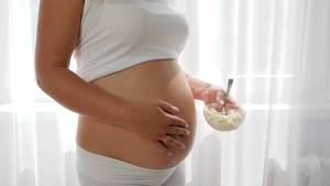 eating pregnant belly nude - sour milk product in the hands of pregnant woman, close-up of future mother