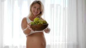 eating pregnant belly nude - portrait of woman with naked abdomen smil and holds dish with fresh fruits  near window -