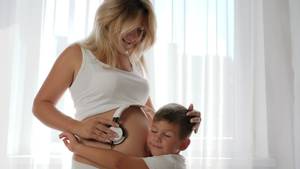 eating pregnant belly nude - boy listens pregnant belly of mother and the woman holds headphones on big naked  tummy and