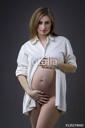 beautiful naked pregnant ladies - Beautiful naked pregnant woman with navel piercing in white shirt on gray  studio background, pregnancy