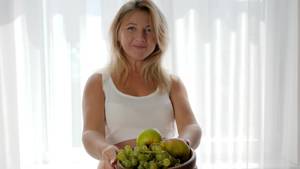 eating pregnant belly nude - woman with baby in belly holds fruits in plate and eats grapes near window,  healthy